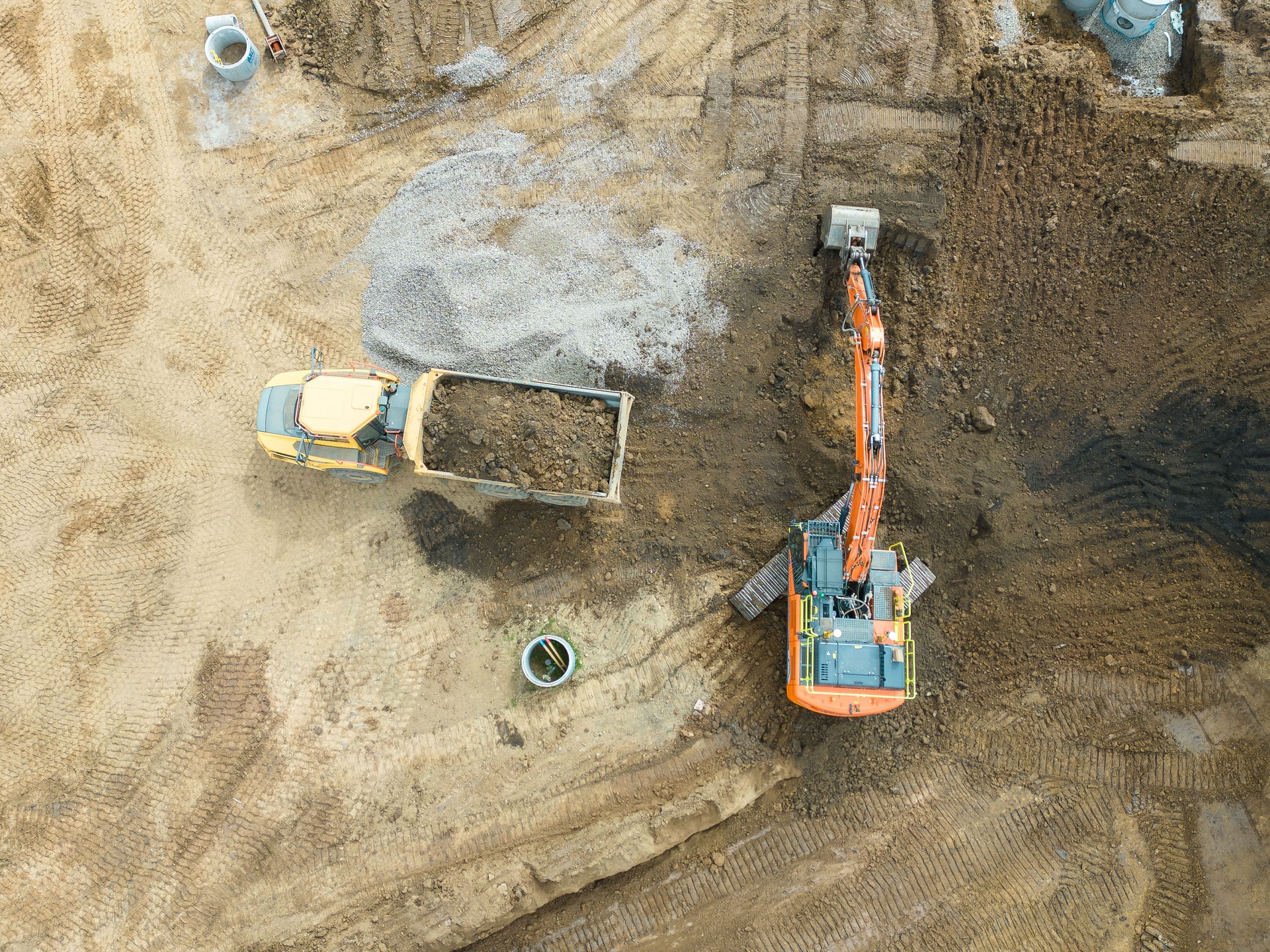 Aerial view of a bulldozer scraping up soil to load onto a dumper truck